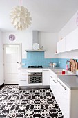 White kitchen cabinets, pale blue wall tiles and black and white cement floor tiles