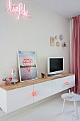 TV and picture on top of white floating sideboard below neon motto on patterned wallpaper