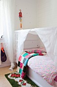 Colourful crocheted blanket, retro rose-patterned rug and child's white bed with canopy