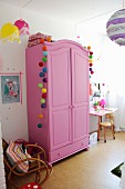 Pink wardrobe decorated with colourful garlands in girl's bedroom