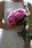 Woman wearing white lace dress holding pink peonies