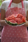 A woman wearing an apron holding a plate of melon slices