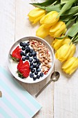 Muesli with yoghurt, blueberries and strawberries next to a bunch of yellow tulips