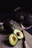 Whole avocados and a halved avocado on a wooden board