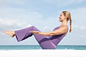 A young blonde woman wearing sports clothes exercising on a beach