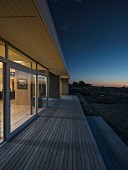 Wooden deck outside contemporary house with illuminated interior at twilight