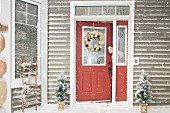 Frau schaut aus geöffneter Haustür in verschneiten Hauseingang