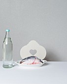 A salmon head on a porcelain plate next to a bottle of water