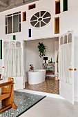 Wall with artistic stained-glass elements and view of white. free-standing bathtub in bathroom