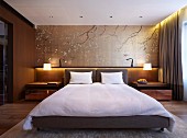Elegantes Schlafzimmer mit Doppelbett und Polsterkopfteil, dahinter Wandgestaltung mit dekorativen, asiatischen Ästemotiven