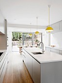 Row of yellow pendant lamps above white island counter in modern kitchen with open terrace doors