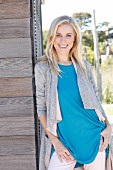 A young blonde woman wearing a blue top and a grey shirt coat