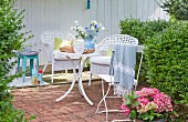 A terrace with white wicker chairs, a folding chair and table in a summery garden