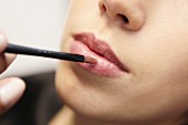 A young woman applying pink lip gloss