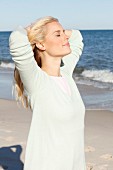 A young blonde woman on a beach wearing a pastel green jumper