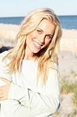 A young blonde woman on a beach wearing a pastel green jumper