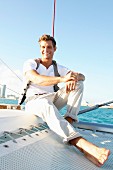 Junger Mann in Freizeitkleidung sitzt auf Segelboot im Meer