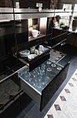 Küchenschrank mit schwarze Hochglanzoberfläche, Kaffeeautomat über offenen Schubladen mit Tassen und Gläsern