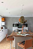 Barhocker mit braunem Lederbezug um Kücheninsel, oberhalb Pendelleuchten mit Retro Keramikschirm in moderner Küche