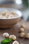 Macadamia nuts in and in front of a wooden bowl