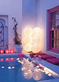 Lit floating candles in pool with purple cushions on side and stacked illuminated paper lanterns in corner