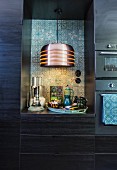 Pendant lamp against patterned wall tiles in niche in black fitted kitchen cupboards