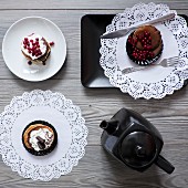 Various dessert tartlets on plates and paper doilies served with tea