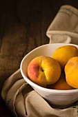 Peaches in a ceramic bowl on a wooden surface