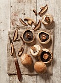 Fresh mushrooms, partially sliced, with an old-fashioned knife on a brown linen cloth