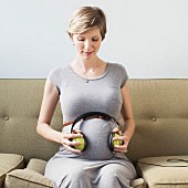 A pregnant woman holding headphones to her tummy