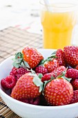 Schale mit Erdbeeren und Himbeeren, dahinter Glas Orangensaft