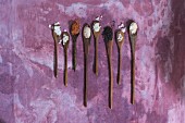 A row of various types of salts on wooden spoons on a purple surface