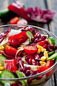A mixed vegetable salad with pomegranate seeds in a glass bowl (close-up)