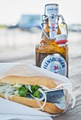 A fish roll and a bottle of beer outside on the table (Sylt, Germany)