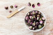 Fresh red Brussels sprouts in a bowl on a wooden surface (seen from above)