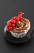 A cupcake topped with chocolate cream and redcurrants