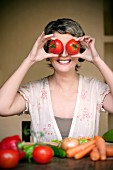 A portrait of a smiling woman holding two tomatoes in front of her eyes