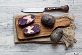 Purple potatoes, whole and halved on a wooden chopping board