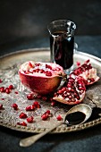 A pomegranate and pomegranate molasses in a glass jug on a silver tray