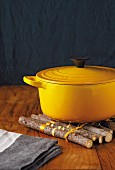 Yellow cast-iron casserole with lid on wooden mat