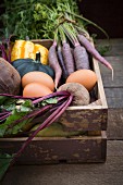 Various organic vegetables and eggs in a wooden crate
