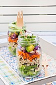 Frühlingshafter Schichtsalat mit Reis, Gemüse und Gänseblümchen in Gläsern auf Tablett