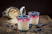 Two glasses of overnight oats with blueberries and berry juice on a wooden surface