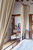 Canopied bed in front of vintage-style dressing table and armchair in renovated farmhouse