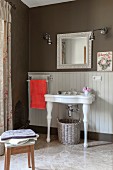 White pedestal sink against wainscoting below mirror with decorated frame in vintage-style bathroom
