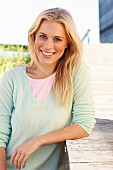 A young blonde woman wearing a pastel green jumper and a pink shirt