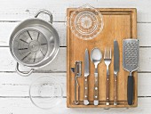 Kitchen utensils: a pot, a measuring jug, a citrus juicer, cutlery, a grater and a peeler
