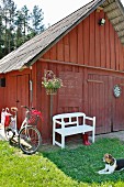White garden bench below hanging basket outside Falu-red barn