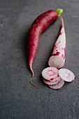 A red radish and a red and white radish on a grey surface