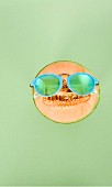 A sliced honeydew melon wearing turquoise sunglasses